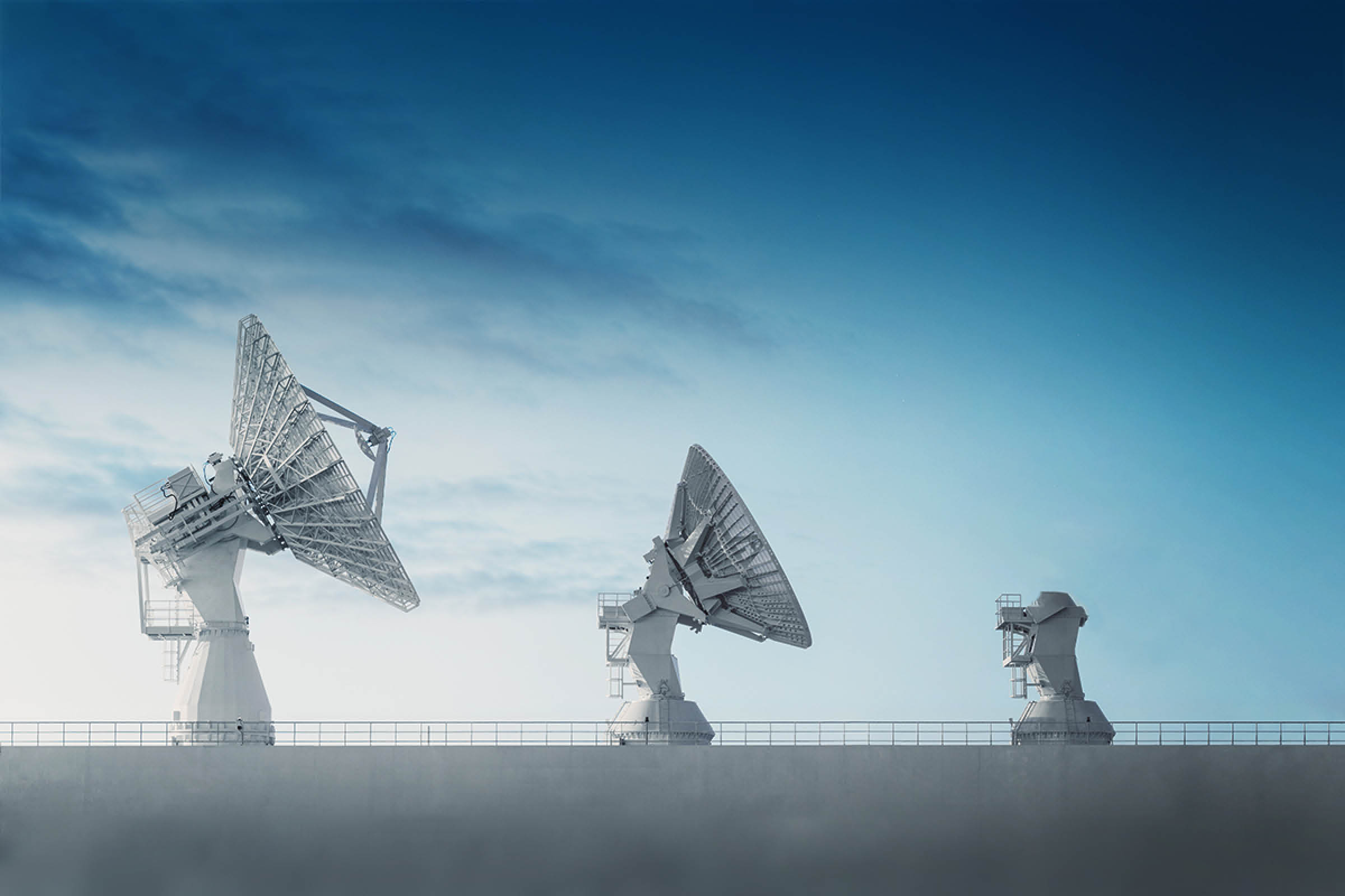 Three satellite dishes perched high atop the deck of a vessel used in tracking rocket trajectories. Long exposure in twilight.